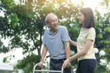 Man using a walker with a woman outdoors in a park setting

