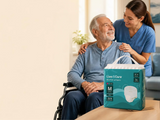 Smiling older man in a wheelchair with a carer, with a pack of Live N Care Adult Pull-Up Pants on the table