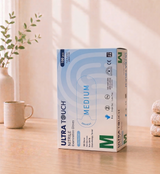 Box of Ultra Touch Nitrile Examination Gloves on a wooden surface with a plant and mug in the background

