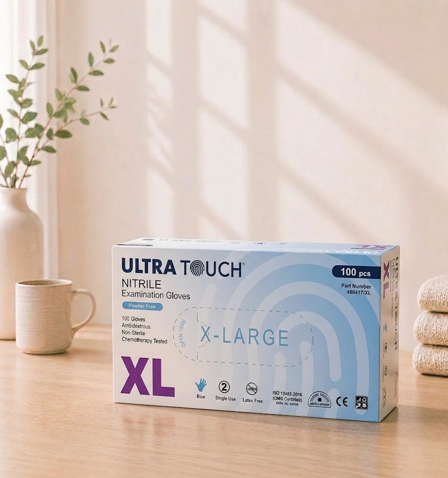 Box of Ultra Touch nitrile examination gloves on a wooden surface with a plant and mug in the background

