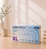 Box of Ultra Touch nitrile examination gloves on a wooden surface with a plant and mug in the background

